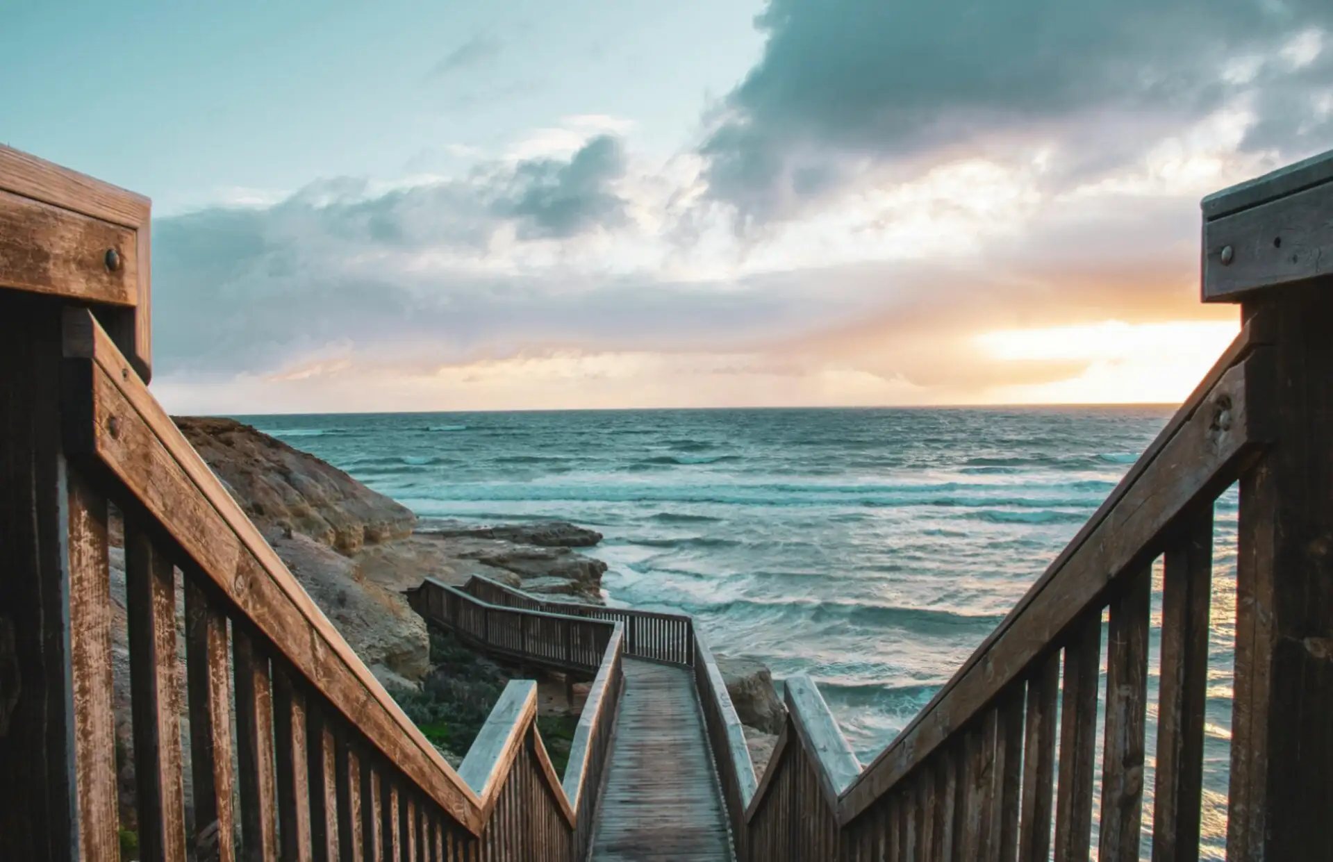 Timber boardwalk stairs leading down to the ocean at sunset