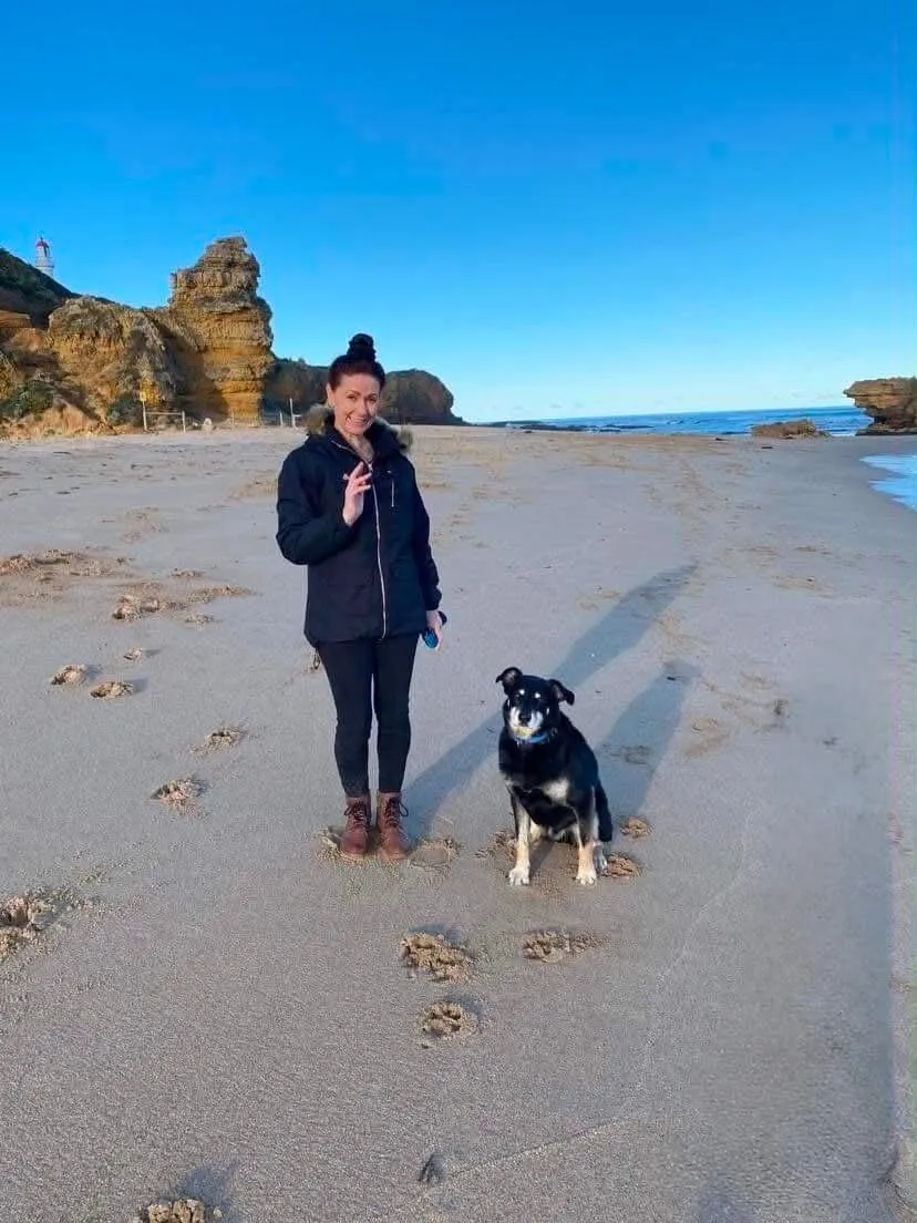 Corrine with her dog on the beach at Aireys Inlet, with the lighthouse and cliffs behind